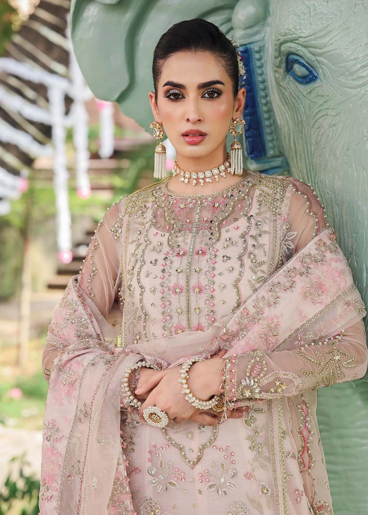 Elevate your style with this light pink organza outfit featuring hand-embroidered panels, dupatta with pallu border, and printed raw silk trouser for a refined look.