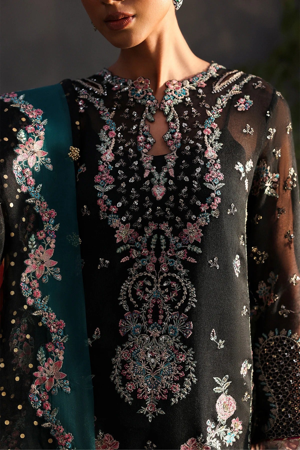 Stunning black khaadi net suit with embroidered panels, green & pink borders, block-printed organza dupatta, and raw silk trouser.