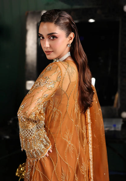 Saffron from Elaf Stardom ’25 features hand-embellished poly-net panels, embroidered dupatta, and raw silk inner — a graceful choice for festive elegance.