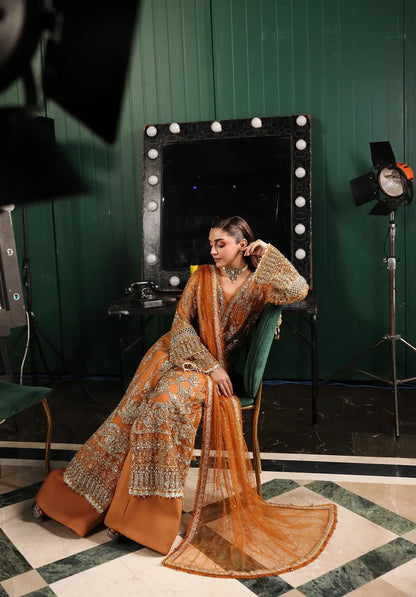 Saffron from Elaf Stardom ’25 features hand-embellished poly-net panels, embroidered dupatta, and raw silk inner — a graceful choice for festive elegance.