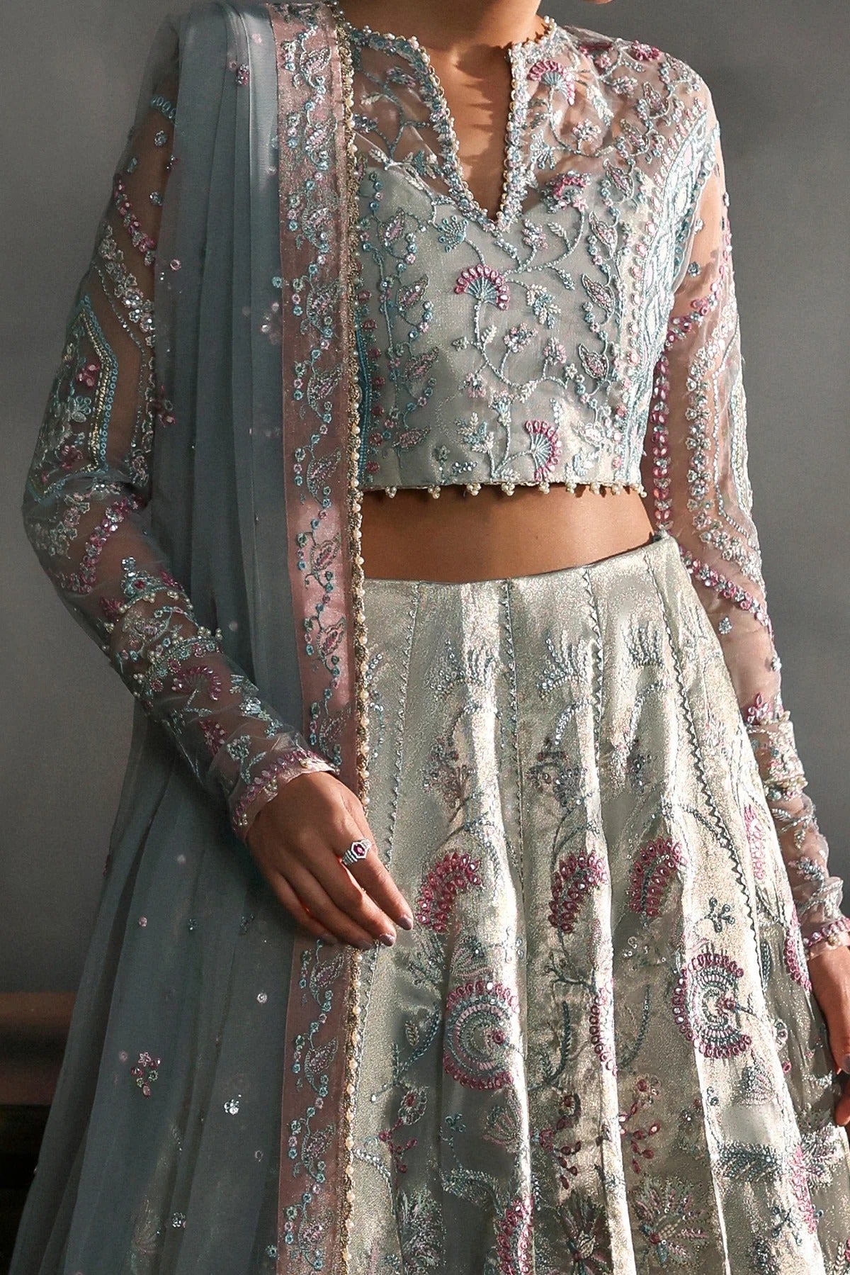 Elegant aqua net dress with intricate zari tissue embroidery in aqua and rose pink. Includes embroidered dupatta, sleeves, and dyed raw silk trouser for grace.