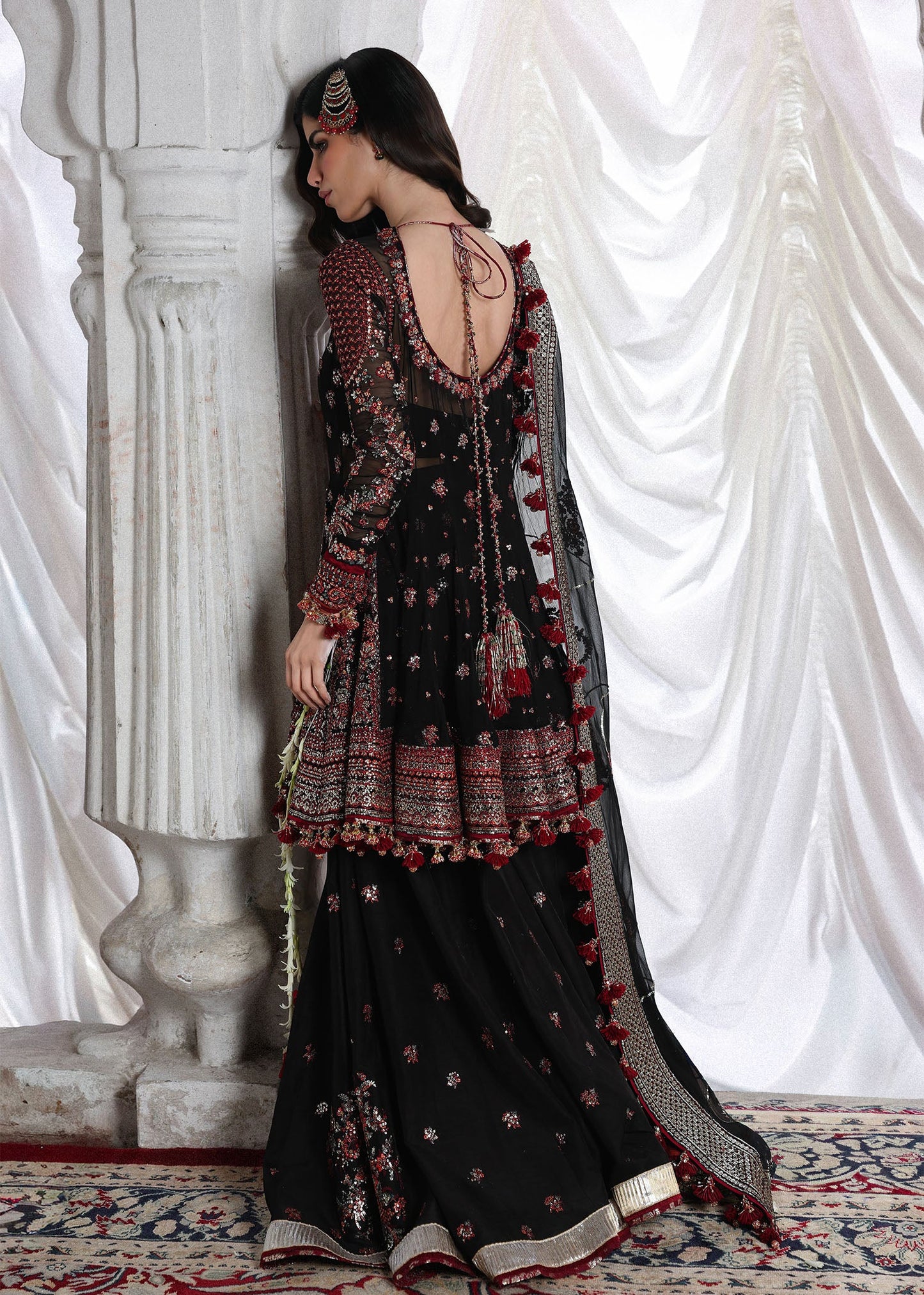 Elegant black embroidered peplum paired with flared Korean raw silk sharara and chiffon dupatta featuring delicate embroidery and four-sided borders for festive events.