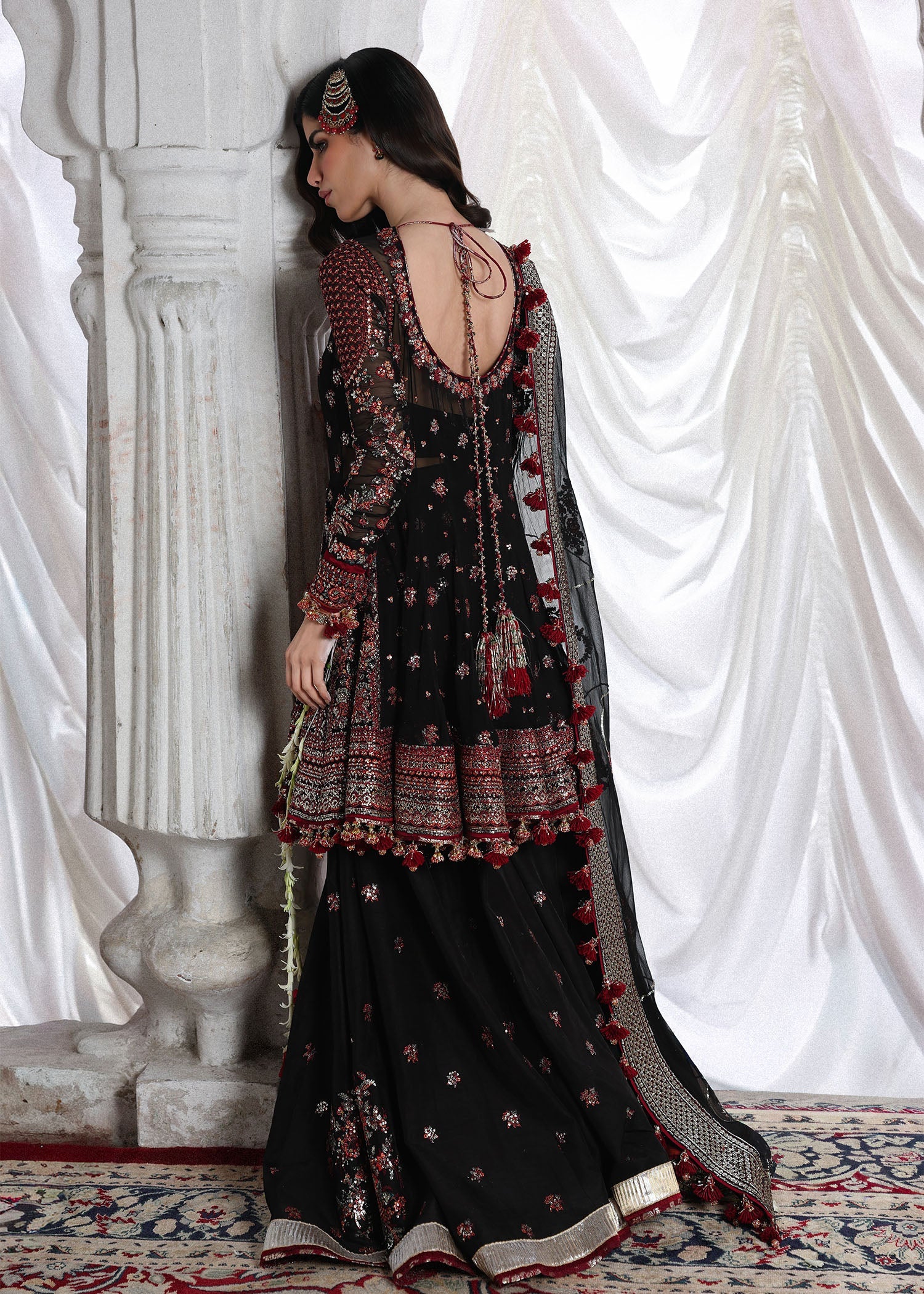 Elegant black embroidered peplum paired with flared Korean raw silk sharara and chiffon dupatta featuring delicate embroidery and four-sided borders for festive events.