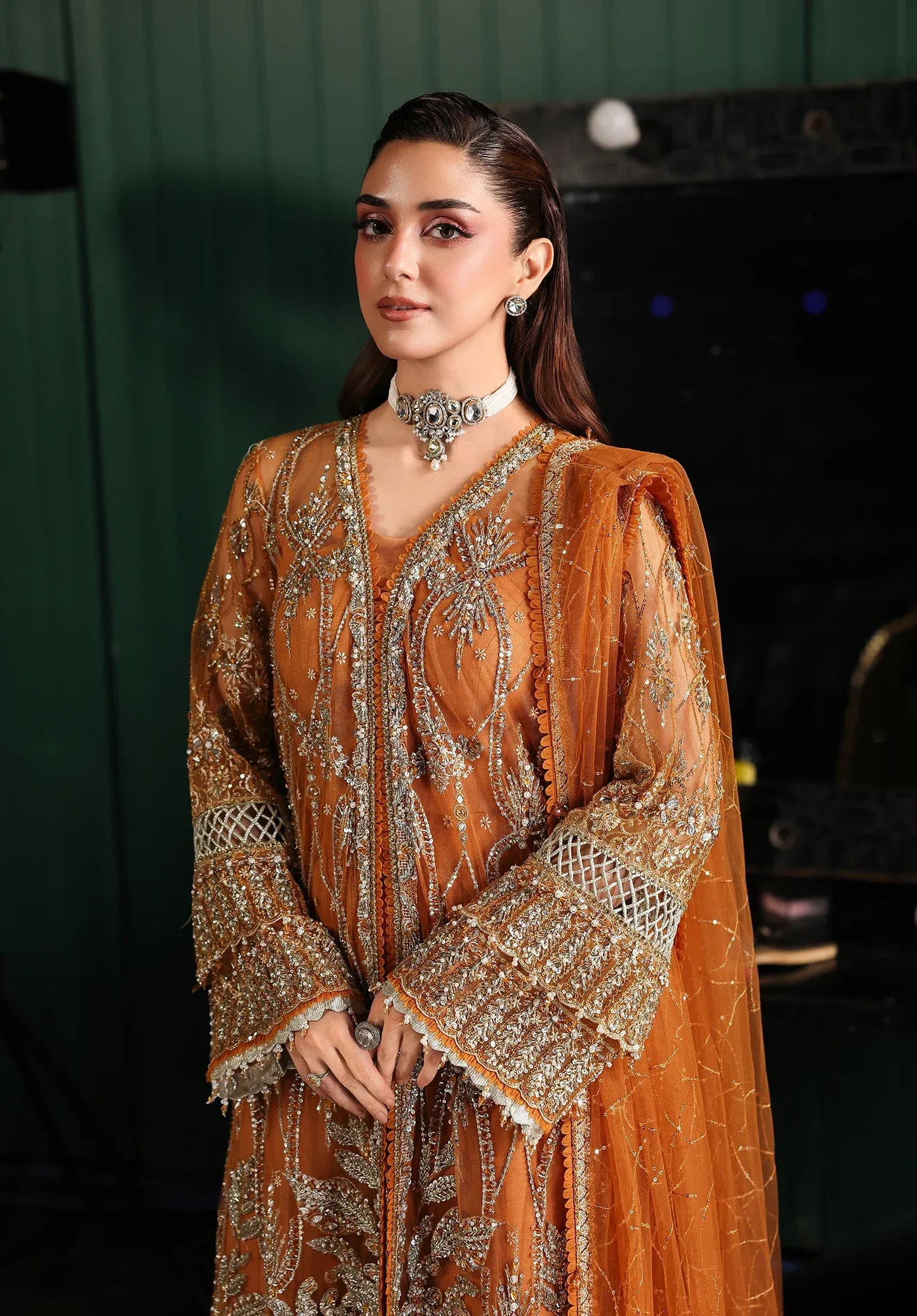Saffron from Elaf Stardom ’25 features hand-embellished poly-net panels, embroidered dupatta, and raw silk inner — a graceful choice for festive elegance.