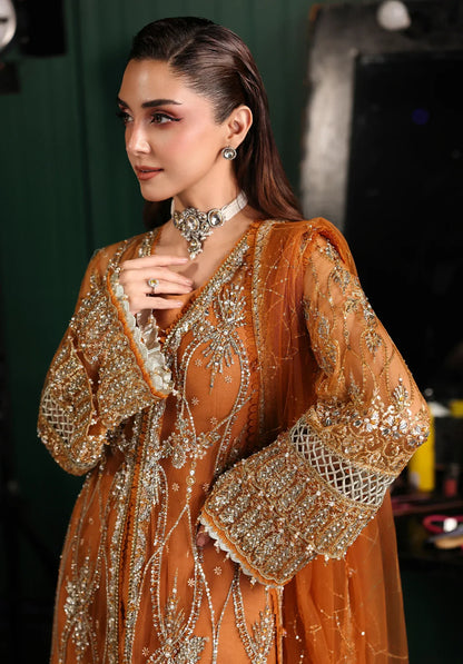 Saffron from Elaf Stardom ’25 features hand-embellished poly-net panels, embroidered dupatta, and raw silk inner — a graceful choice for festive elegance.