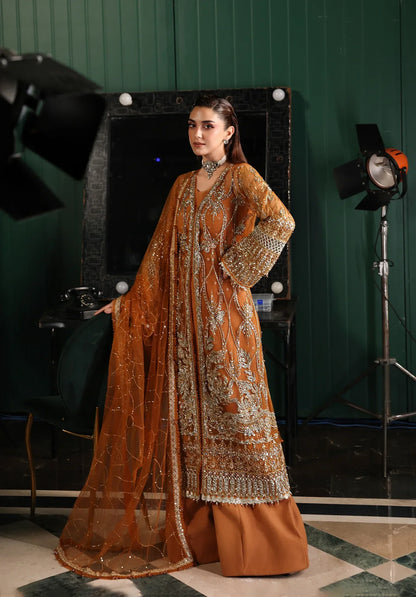 Saffron from Elaf Stardom ’25 features hand-embellished poly-net panels, embroidered dupatta, and raw silk inner — a graceful choice for festive elegance.