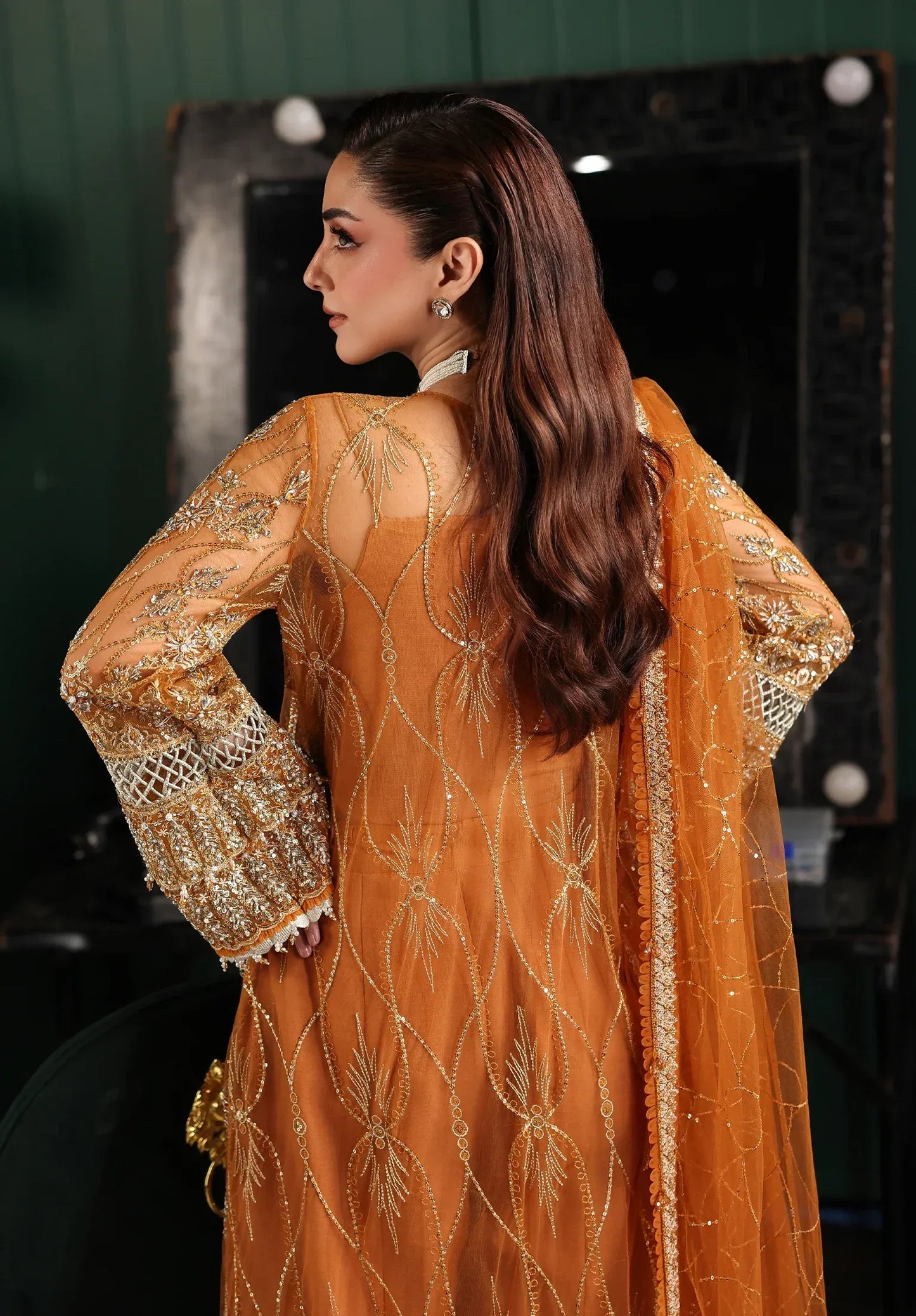 Saffron from Elaf Stardom ’25 features hand-embellished poly-net panels, embroidered dupatta, and raw silk inner — a graceful choice for festive elegance.