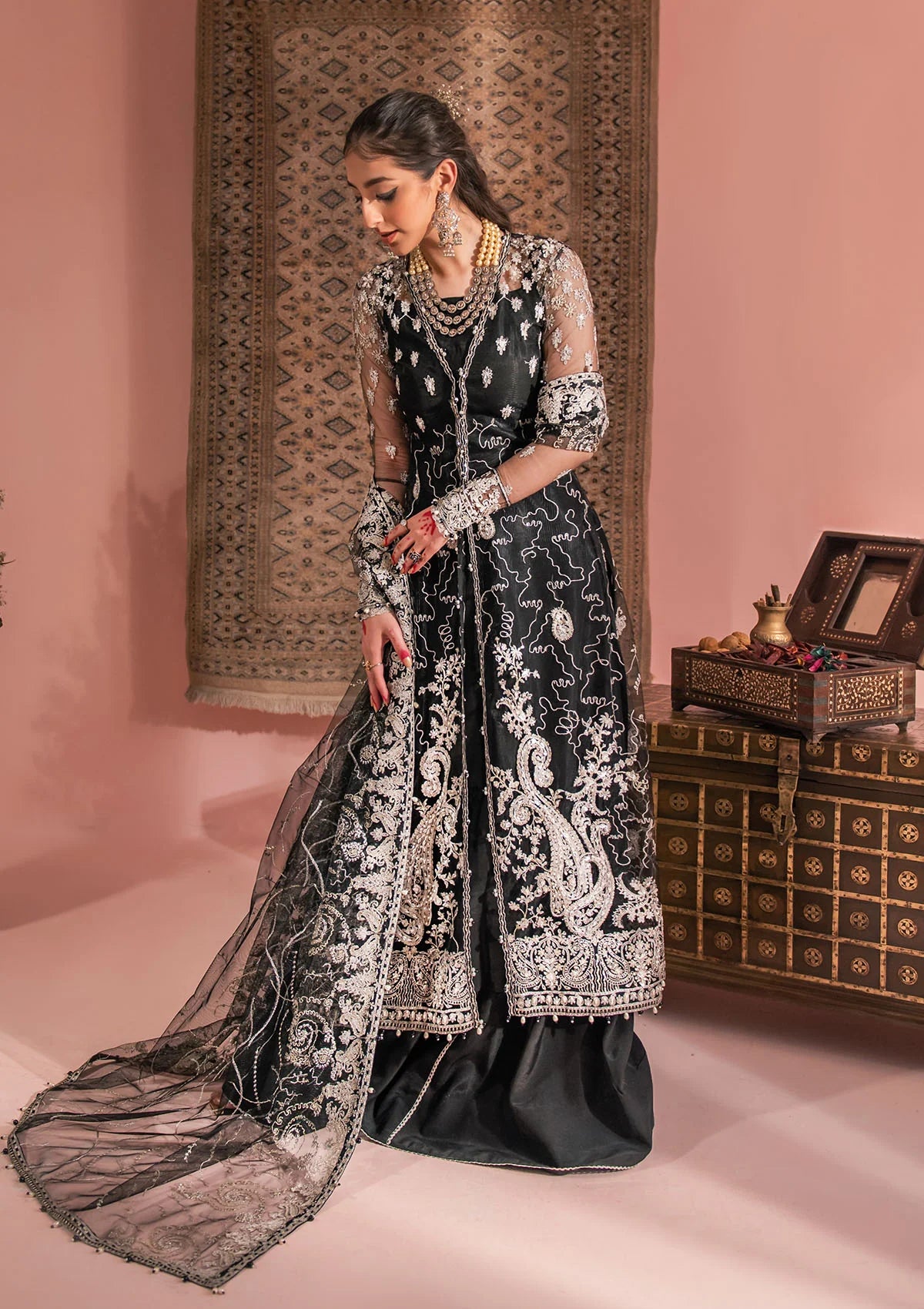 Timeless black net ensemble featuring Kashmiri paisley motifs, refined sequin and bead embellishments, organza borders, raw silk pants, and an embroidered net dupatta for elegant monochrome appeal.