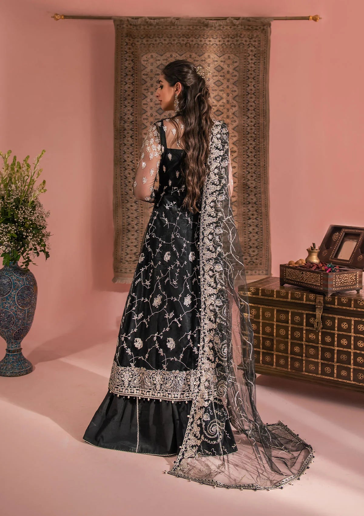 Timeless black net ensemble featuring Kashmiri paisley motifs, refined sequin and bead embellishments, organza borders, raw silk pants, and an embroidered net dupatta for elegant monochrome appeal.