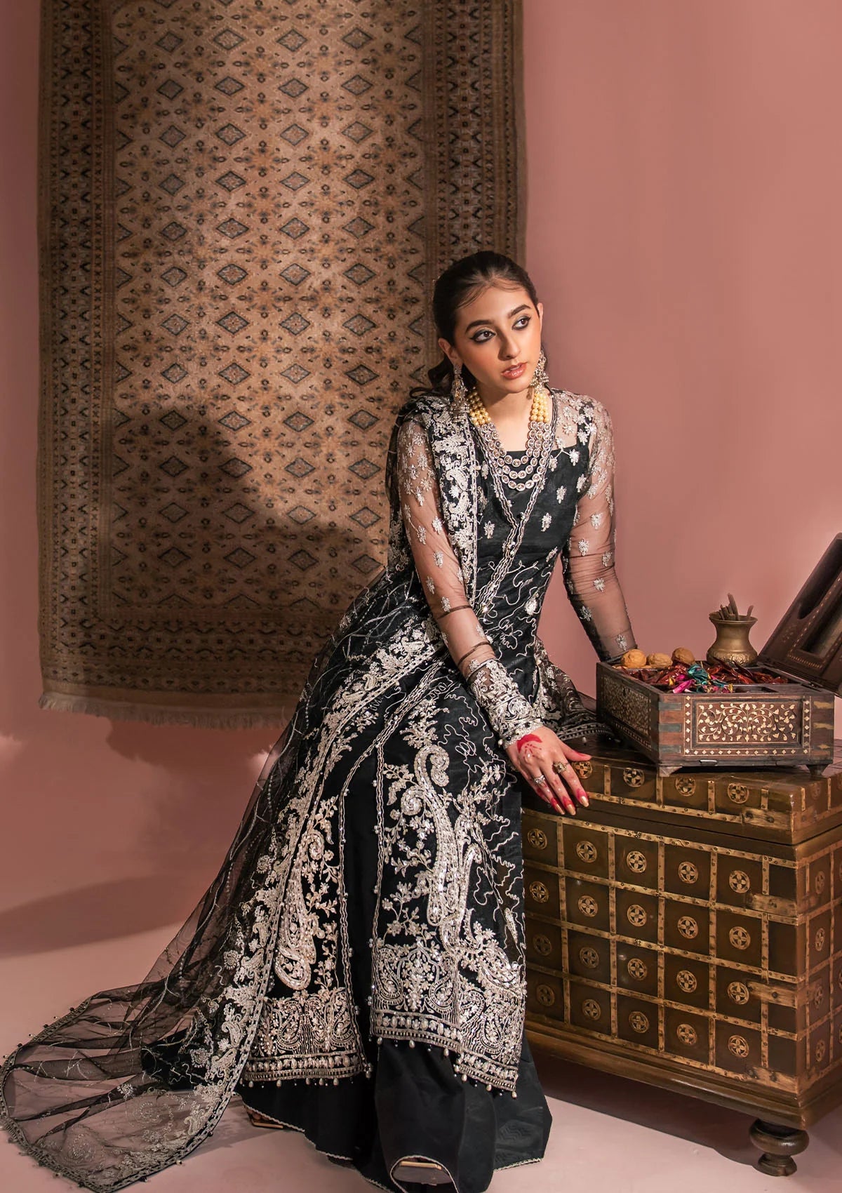 Timeless black net ensemble featuring Kashmiri paisley motifs, refined sequin and bead embellishments, organza borders, raw silk pants, and an embroidered net dupatta for elegant monochrome appeal.