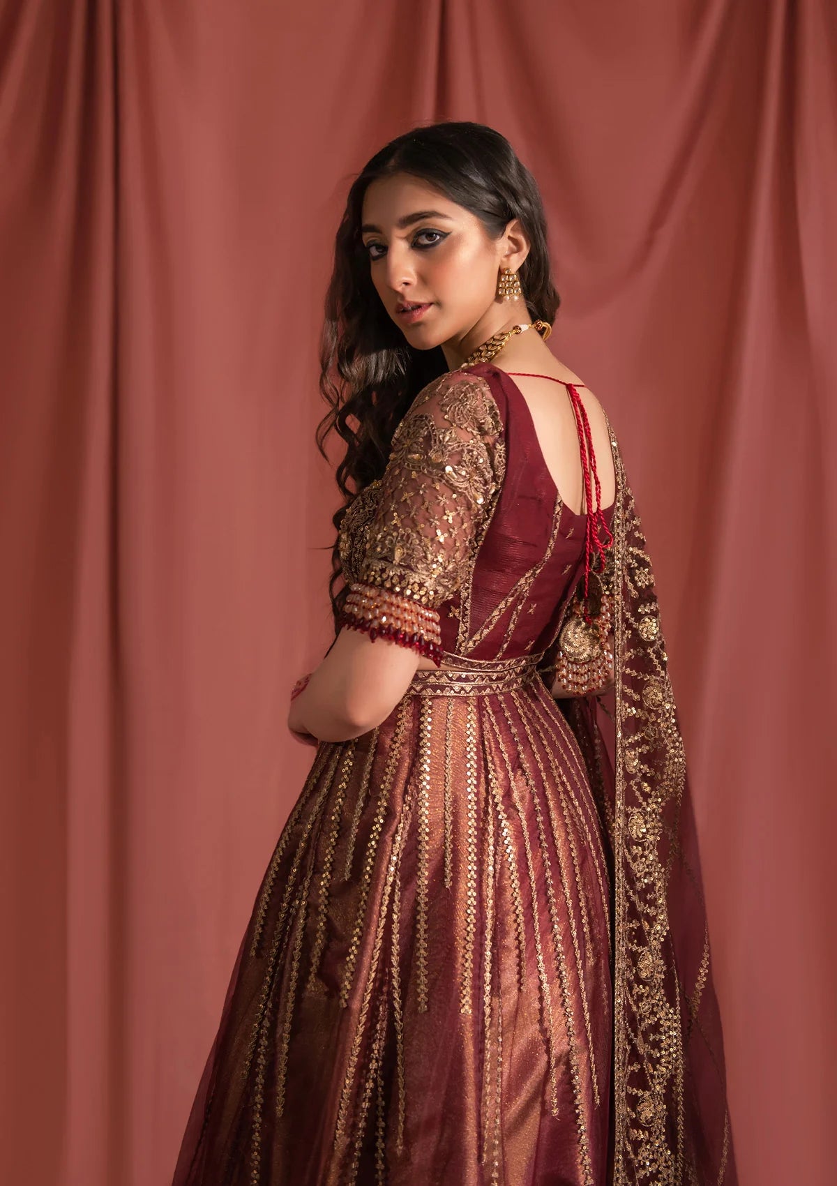 Festive mahogany net ensemble inspired by Kashmiri craftsmanship, featuring oxidised gold and bronze tilla, antique sequins, hand embellishments, masoori silk pants, and an embroidered net dupatta.