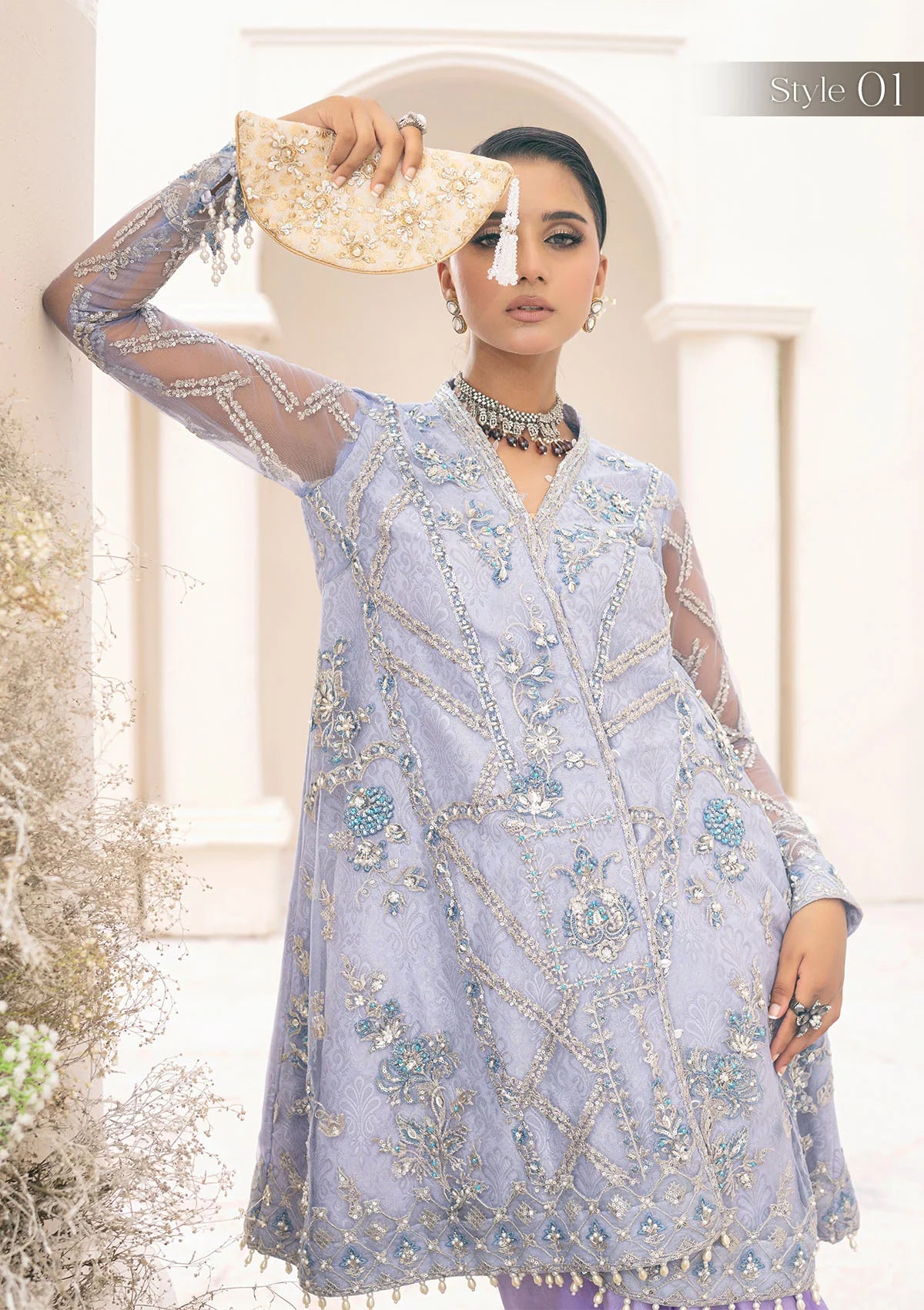Exquisite lavender net ensemble featuring crystal and pearl embellishments, tilla-infused embroidery, masoori silk pants, and an organza jacquard dupatta. Styled as a short shirt with draped skirt or long shirt with sharara pants.