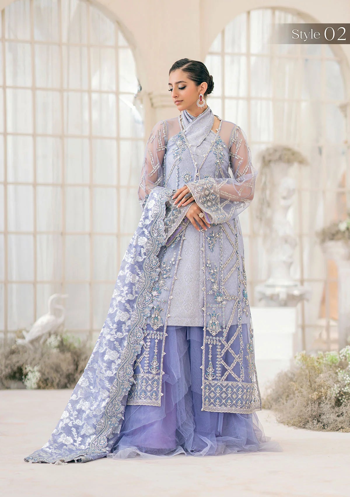 Exquisite lavender net ensemble featuring crystal and pearl embellishments, tilla-infused embroidery, masoori silk pants, and an organza jacquard dupatta. Styled as a short shirt with draped skirt or long shirt with sharara pants.