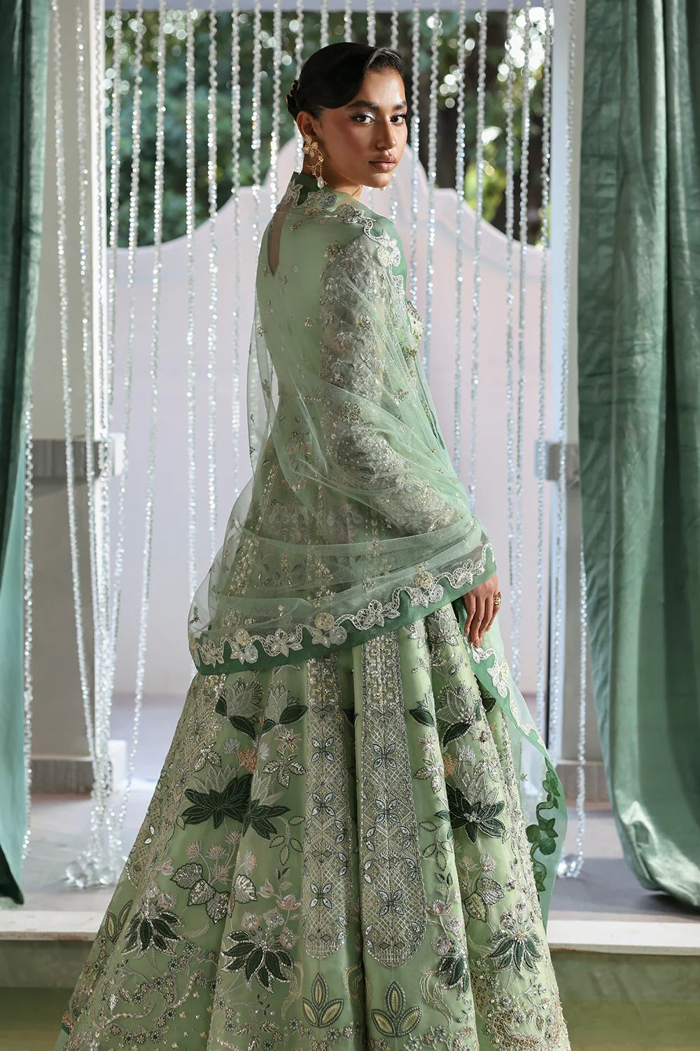Elegant mint green silk suit featuring embroidered organza panels, velvet neck patch, net dupatta, and silk trousers. 