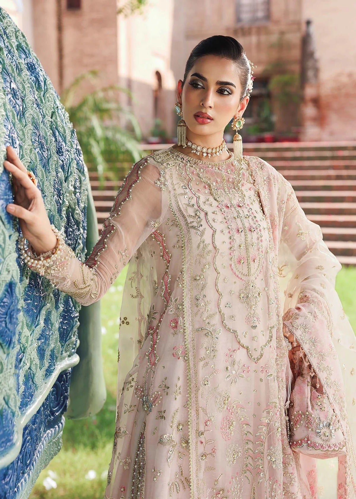 Elevate your style with this light pink organza outfit featuring hand-embroidered panels, dupatta with pallu border, and printed raw silk trouser for a refined look.