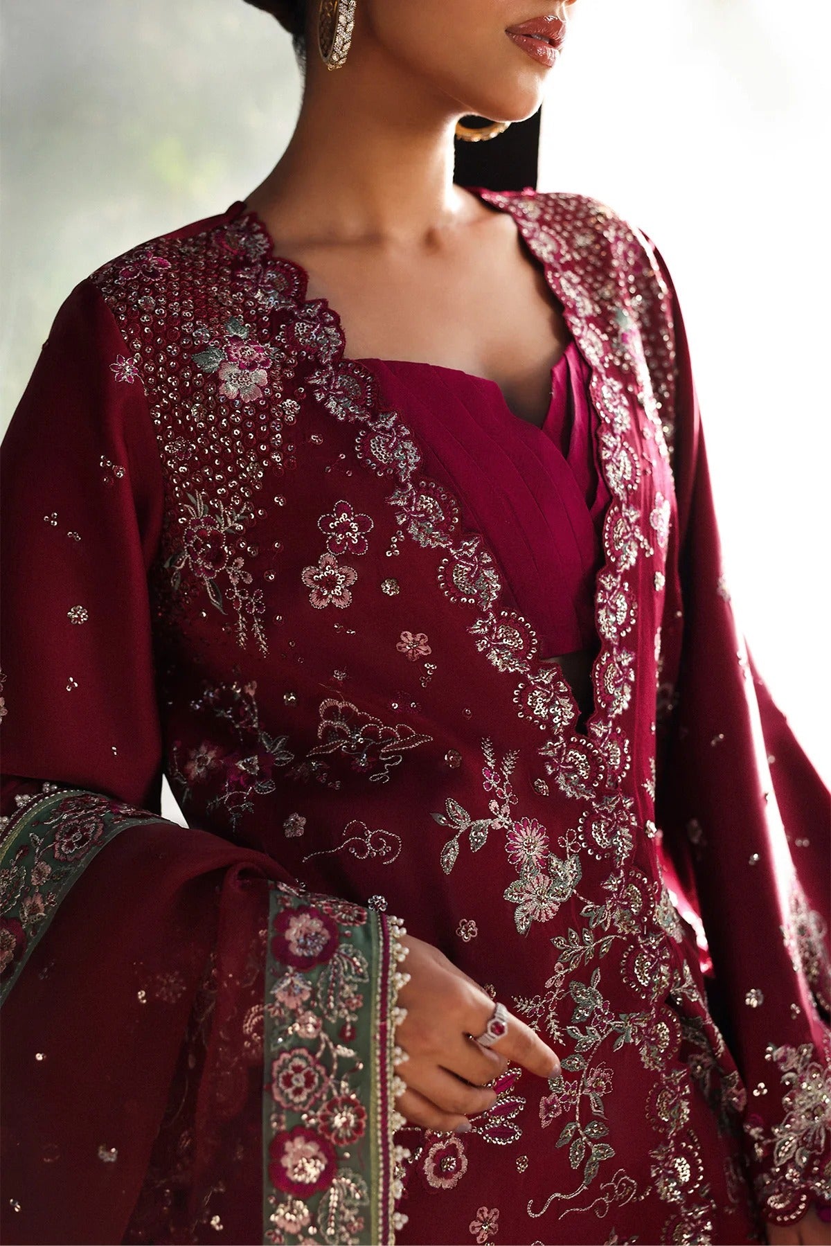 Striking cherry raw silk suit with embroidered panels, green organza dupatta border, and matching trouser for a bold festive look.